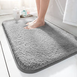Light gray flannel absorbent bathroom floor mat placed in front of a shower on white tile