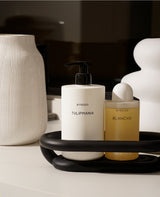 Matte black Nordic bathroom storage tray holding skincare bottles and cotton rounds on a counter