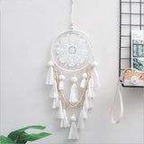 Romantic decorative wall dream catcher with wooden beads and tassel hanging above a bedroom headboard