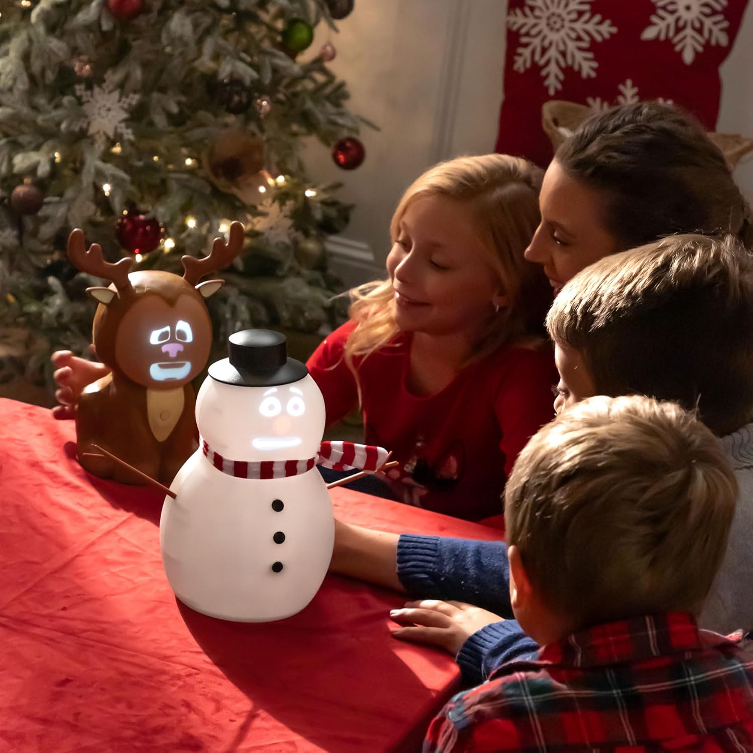 Family gathered around a snowman-shaped light with a reindeer decoration in front of a Christmas tree.