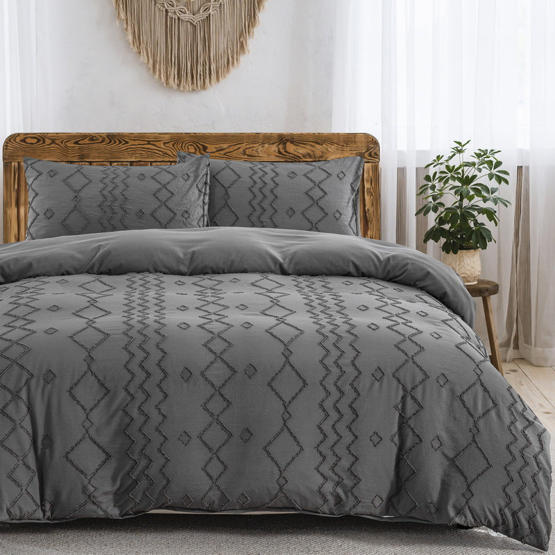 Gray patterned bedding set on a bed in a bedroom with a wooden headboard and decorative wall hanging.
