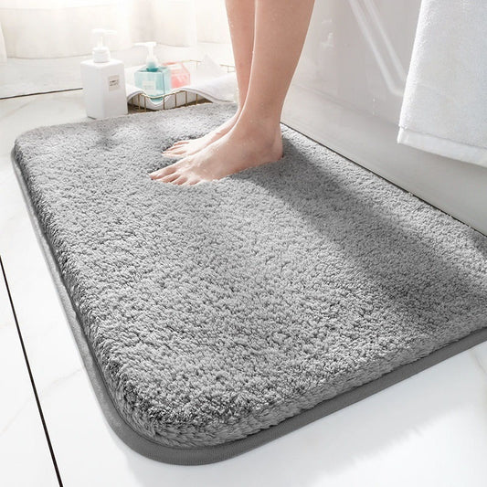 Light gray flannel absorbent bathroom floor mat placed in front of a shower on white tile
