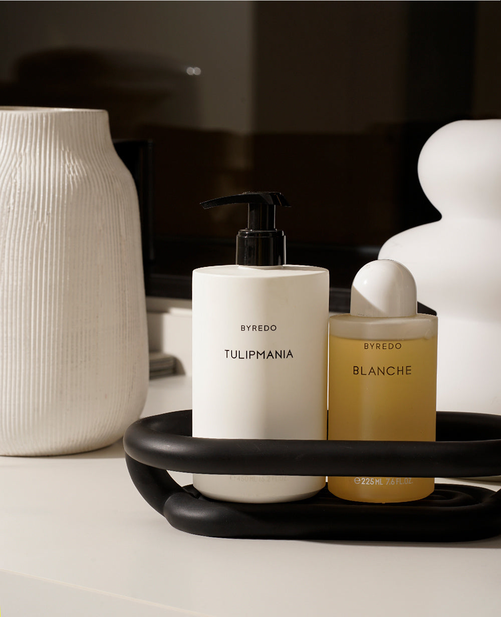 Matte black Nordic bathroom storage tray holding skincare bottles and cotton rounds on a counter
