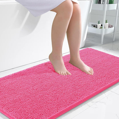Pink soft chenille bathroom mat placed in front of a bathroom sink on light tile floor
