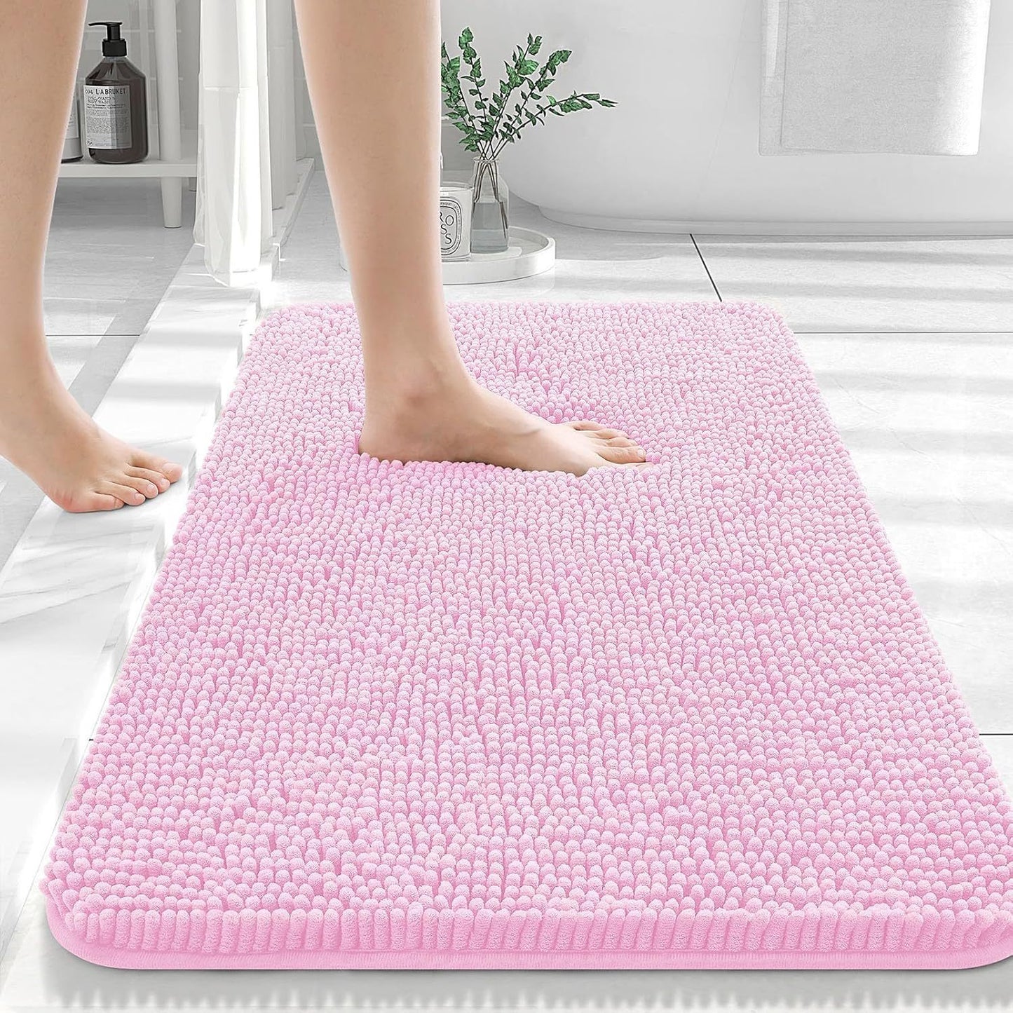 Pink soft chenille bathroom mat placed in front of a bathroom sink on light tile floor
