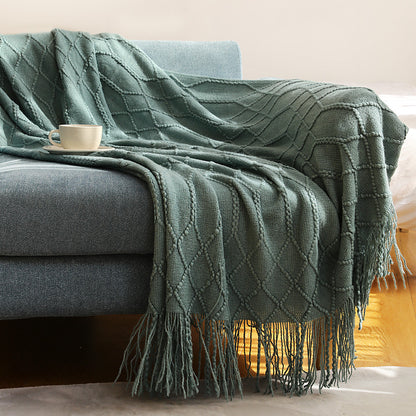 Khaki coral fleece blanket bundled in a reading nook chair beside a small lamp and book
