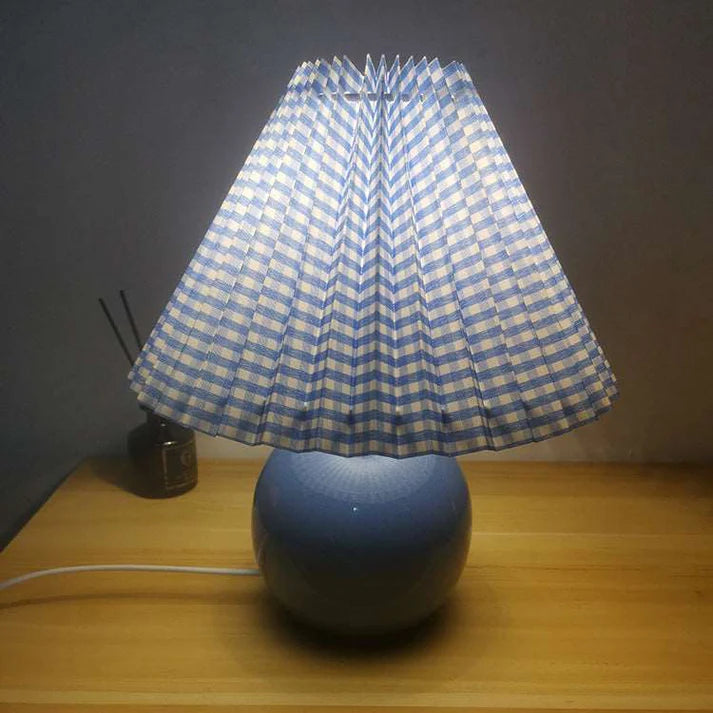 Decorative bedroom lamp with blue ceramic base and pleated fabric shade on side table

