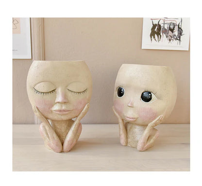 Two face head sculpture planters with flowers on table