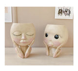 Two face head sculpture planters with flowers on table