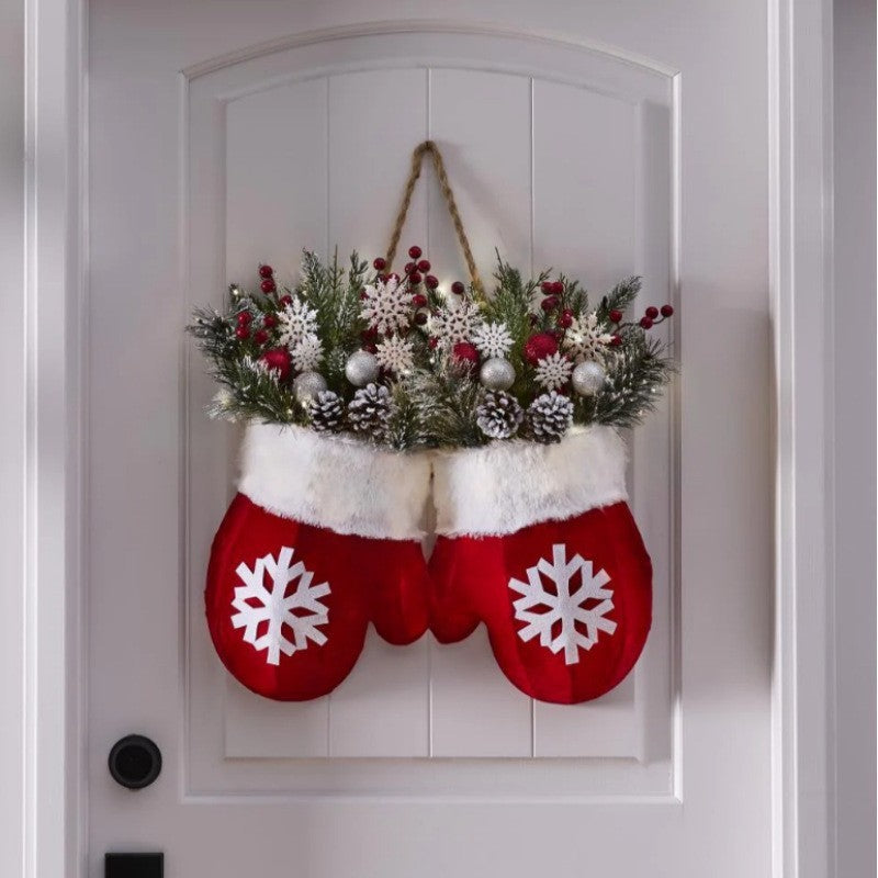Decorative red mittens with white snowflakes holding a festive wreath on a white door.