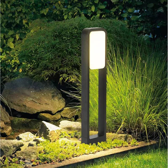 Aluminum lawn lamp glowing in garden at night beside rocks
