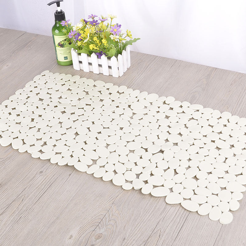Eco friendly pebble PVC bath mat placed outside a bathtub on white bathroom tile
