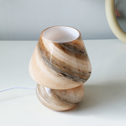 Beige retro glass bedside table lamp with warm light on a wooden nightstand
