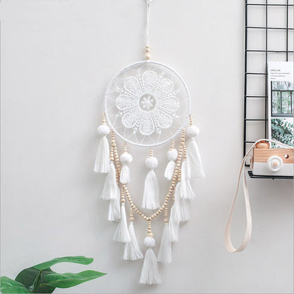 Romantic decorative wall dream catcher with wooden beads and tassel hanging above a bedroom headboard
