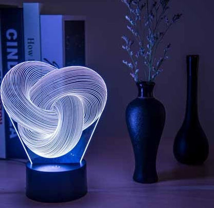 Twist abstract 3D acrylic LED night light glowing blue on a bedroom nightstand in the dark
