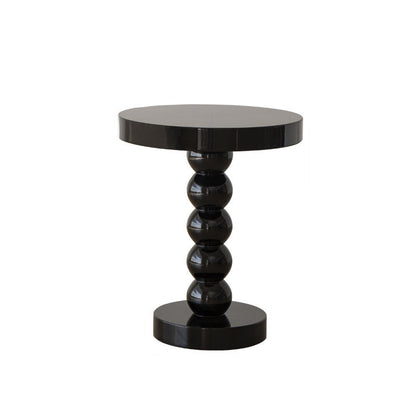Vintage solid wood round side table holding a lamp, book, and phone as a bedside surface
